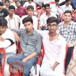 Group of young men sitting on red chairs at an outdoor school event; Heritage International School logo visible bottom left.