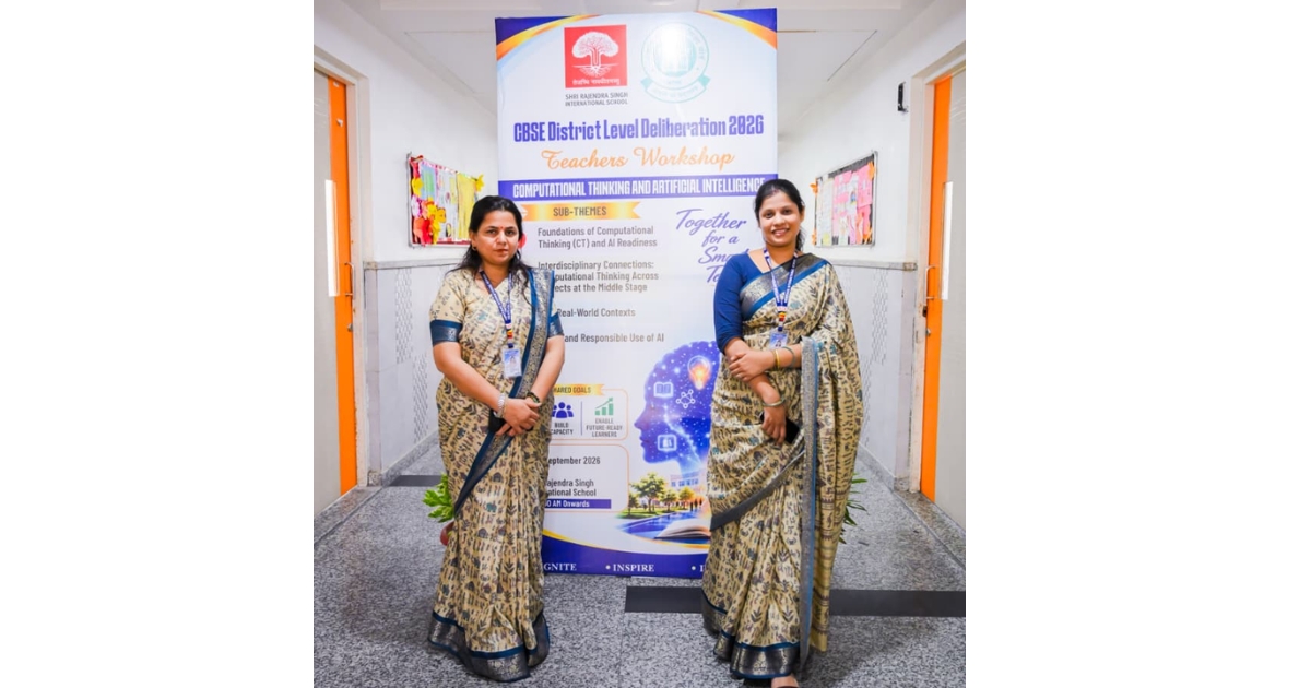 Two women in sarees with lanyards stand in a school hallway beside a large banner for a CBSE district-level teachers' workshop interpretation of computational thinking and AI topics.
